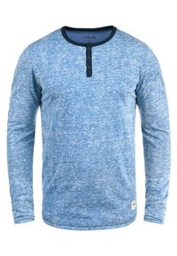 Chemise henley à manches longues bleue avec une finition texturée. Elle présente un col rond bleu marine et trois boutons sombres au niveau du col. Motif subtilement chiné.