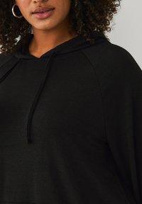 Sort hætte sweatshirt med tekstureret stof, snor og raglanærmer, designet til en afslappet pasform.