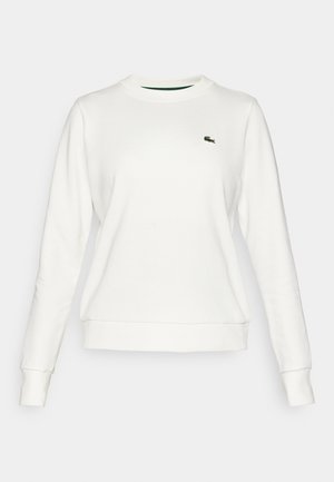 Sweatshirt branco com gola redonda, mangas longas e punhos canelados. Apresenta um pequeno logótipo Lacoste bordado em verde no peito esquerdo.