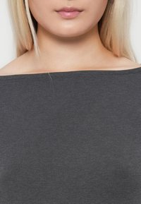 Sivi, bijeli top bez naramenica izrađen od mekog pamučnog materijala. Ima jednostavan dizajn s ravnim izrezom, bez vidljivih uzoraka ili naglasaka.