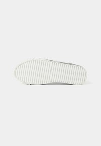 Weiße Gummisohle mit horizontalen Rillen und erhabenem Muster entlang der Ränder. Glatte Textur mit minimalistischem Design.