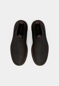 Braune Slipper mit einer glatten, matten Oberfläche, elastischen Seitenpaneelen und einem runden Zehendesign. Verfügt über eine strukturierte Gummisohle für besseren Grip.