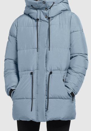 Light blue quilted puffer jacket with hood, black drawstrings, side pockets, and hands tucked in pockets, worn with black pants.