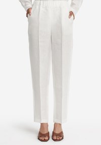 Linnedbukser i hvid med løs pasform, der har en taljebånd og sidelommer. Kombineret med brune åbne slide-sandaler.