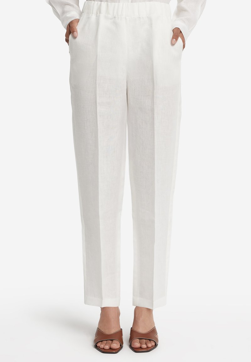 Linnedbukser i hvid med løs pasform, der har en taljebånd og sidelommer. Kombineret med brune åbne slide-sandaler.