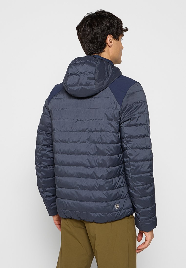 Doudoune en marine foncé avec un motif matelassé horizontal, capuche attachée et panneaux d'épaule contrastants ; présente un détail de logo à l'ourlet.