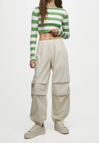Grüner und weißer gestreifter, cropped Pulli mit langen Ärmeln, kombiniert mit beigen, lockeren Cargo-Hosen, die schmal zulaufen. Sie verfügen über einen elastischen Bund und Taschen.