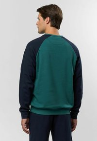 Kreklu apakšējais svītra ar zaļu korpusu un tumši zilu raglanu piedurknēm. Mīksts audums, ribotas aproces un apakšmala, minimālas šuvju detaļas.