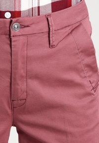 Dark pink cotton pants featuring a flat front, side pockets, and a single metal button closure. Smooth texture with subtle stitching details.
