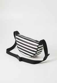 Bolso bandolera a rayas en blanco y negro, hecho de material brillante, con cierre de cremallera y correa negra ajustable. Forma redondeada.