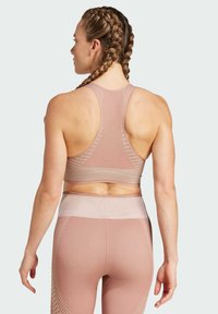 Sujetador deportivo en color rosa empolvado con un diseño de espalda nadadora, que presenta líneas horizontales y verticales texturizadas. Tejido suave con un ajuste ceñido.