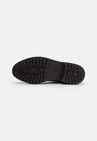 Talpa de pantof din cauciuc negru cu șanțuri adânci, având modele în diamant și dreptunghiulare pentru aderență, și un logo modelat în centru.
