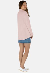 Langärmlige, hellrosa Bluse mit Kragen, strukturiertem Stoff und Knopfmanschetten, kombiniert mit einem Jeans-Minirock und weißen Schuhen.