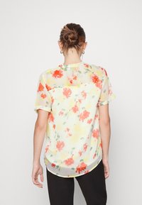 Květinová blůza v světle žluté barvě se vzory červených a oranžových květin. Lehká, s krátkým rukávem, kulatým lemem. Průsvitná látka s volným střihem.