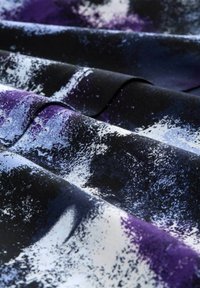 Textilstoff mit einer glatten Struktur zeigt ein gewagtes abstraktes Muster in Schwarz, Lila und Blau, das einen dynamischen visuellen Effekt erzeugt.
