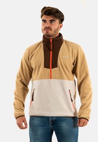 Sudadera de forro polar en tono tostado y blanco con cuello marrón, cremallera naranja y dos bolsillos laterales con cremallera. Cuenta con un diseño de cremallera de cuarto y una textura suave.