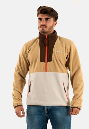 Pullover in pile color sabbia e bianco con colletto marrone, zip arancione e due tasche frontali con zip. Presenta un design a zip quarti e una texture morbida.