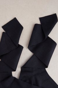 Schwarzer gestrickter Stoff mit einer glatten Textur, der lange, fließende Bänder aufweist, die in einer geschichteten Anordnung gewunden sind.