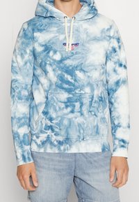Pullover hoodie in blue tie-dye pattern, made of soft fabric with a front pocket, adjustable drawstring hood, and ribbed cuffs.