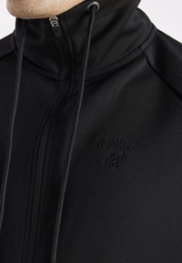 Felpa nera con zip e colletto alto, dotata di logo ricamato, texture liscia e cordino regolabile per la chiusura.