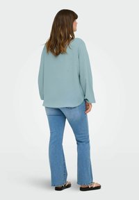 Svetlo modra majica z dolgimi rokavi in okroglim izrezom, sproščenega kroja in mehke teksture, v kombinaciji s svetlo modrimi širokimi jeans hlačami in črnimi sandali.