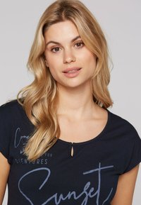 Navy blue t-shirt with short sleeves, round neckline, and a keyhole detail. Features light-colored text: "Come for Adventures" and "Sunset."