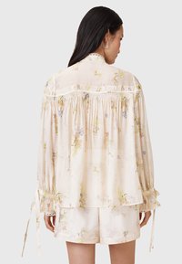 Helle cremefarbene Bluse mit floralem Muster, weitem Schnitt, Puffärmeln und gerafften Details; verfügt über Bindebänder an den Manschetten und Spitzenbesatz.
