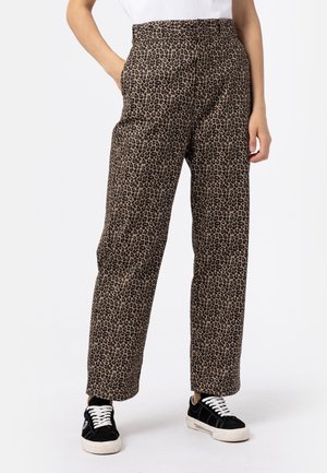 Leopardmønstret bukser med lige ben, båret med sort-hvide sneakers og en hvid top, hænder afslappet langs siden.