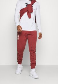 Czerwone dresy z elastycznymi mankietami i logo na nogawce, w połączeniu z białą koszulką z długim rękawem z czarnym logo oraz czerwoną bluzą związana na ramionach.