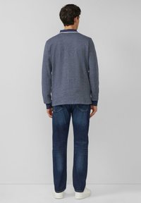 Granatowa koszulka polo z długim rękawem o teksturowanym wykończeniu i kontrastującym kołnierzem, zestawiona ze średnio wypranymi dżinsami i białymi trampkami.