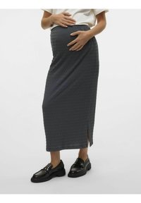 Jupe midi plissée grise avec une fente sur le côté, fabriquée en tissu texturé. Associée à des mocassins noirs avec une semelle épaisse.