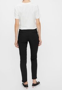 Svarta slim-fit byxor med en slät textur, kombinerat med en vit t-shirt med kort ärm. Outfiten inkluderar avslappnade svarta sneakers.