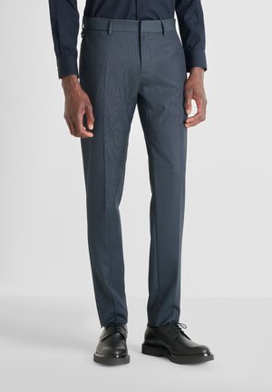 Pantalones oscuros grises a medida con un sutil patrón de cuadros, fabricados en tela tejida. Con frente plano, trabillas para cinturón y diseño de corte ajustado. Zapatos de vestir negros.