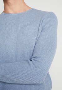 Ljusblå stickad tröja med rund halsringning och mönstrad yta. Långa ärmar med en figurnära design som framhäver det mjuka tyget.