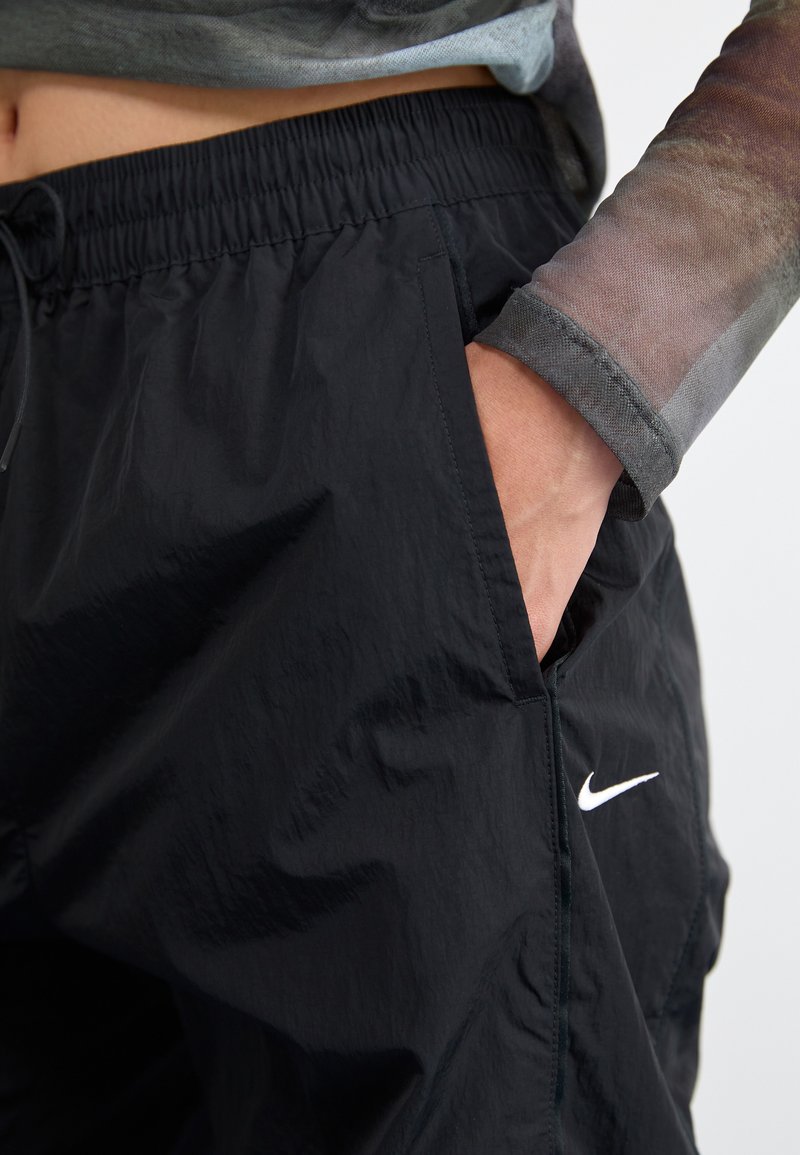 Shorts de sport noirs avec une taille élastique, dotés de poches latérales et d'un logo Nike blanc. Tissu lisse et léger avec une légère brillance.