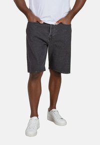 Pantalones cortos de mezclilla negra con corte recto, un bolsillo frontal y trabillas para cinturón. Se llevan con una camiseta blanca y zapatillas blancas.