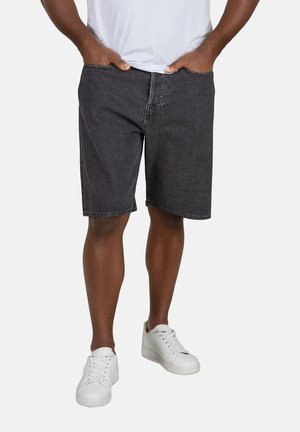 Schwarze Jeansshorts mit geradem Schnitt, einer vorderen Tasche und Gürtelschlaufen. Tragen mit einem weißen T-Shirt und weißen Turnschuhen.