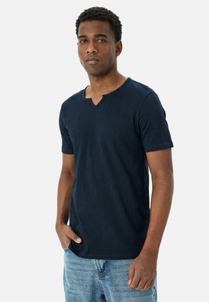 Camisa de cuello en V de manga corta color azul marino con superficie texturizada. Presenta un pequeño detalle de botón en el cuello y una silueta ajustada.
