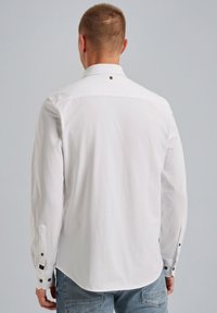 Weißes Langarmhemd mit geknöpftem Kragen, ausgestattet mit schwarzen Knopfakzenten an den Manschetten und einem kleinen Logodetail in der Nähe des Halsausschnitts.