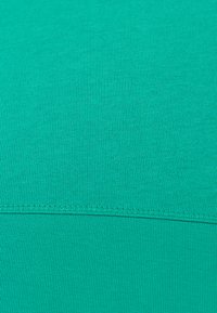 Een levendige teal stof met een gladde, gestructureerde oppervlakte, voorzien van een fijn geribd patroon en versterkte stiksels langs de zoom.