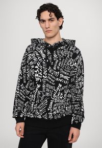 Sweatshirt à capuche noir avec impression de texte blanc dans divers styles. Présente une capuche avec cordon de serrage et des poignets et un ourlet côtelés. Texture de tissu douce.