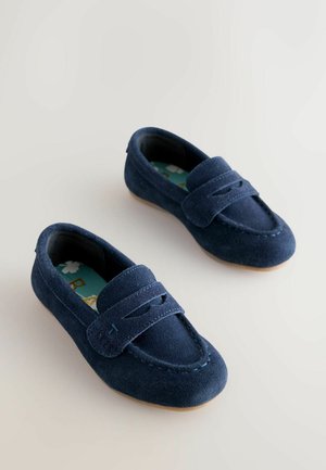 Námořnicky modré semišové mokasíny s prošívanými detaily, ozdobným páskem přes nárt a světle hnědou gumovou podrážkou. Měkká textura po celém povrchu.