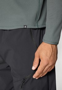Chemise grise texturée à manches longues avec un motif côtelé et pantalon léger noir avec une poche zippée.