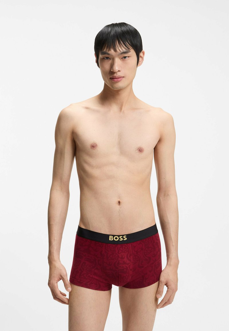 Boxer rouge à motifs avec une ceinture noire ornée de l'inscription "BOSS" en lettres dorées, fabriqué dans un matériau doux et extensible.