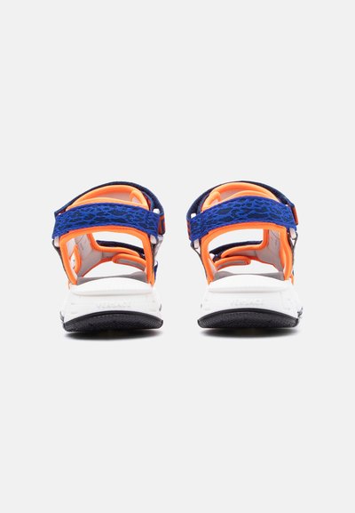 Ζευγάρι αθλητικών σανδαλιών με μπλε λουράκια σε λεοπάρ μοτίβο, πορτοκαλί λεπτομέρειες και λευκές μαξιλαρωτές σόλες, που φαίνονται από πίσω.