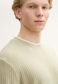 Hellbeige strukturierter Sweatshirt mit feinem Karomuster, Rundhalsausschnitt und gerippten Bündchen. Hergestellt aus weichem, atmungsaktivem Material.