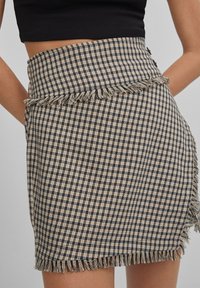 Beżowo-granatowa w kratę mini spódnica z frędzlami u dołu, z dopasowanym stanem i bocznymi guzikami.