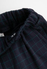 Granatowa tkanina w kratę z zielonym wzorem w kratkę, z elastycznym paskiem i zapięciem na guzik. Miękka tekstura, odpowiednia do codziennego noszenia.