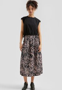 Top nero a maniche corte con vita regolabile e una lunga gonna a stampa zebra rosa e nera con tasche. Indossato con stivali neri alla caviglia.