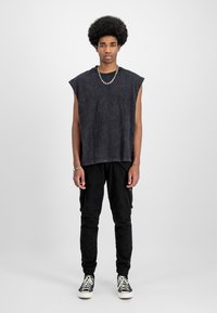 Cămașă neagră, fără mâneci, supradimensionată, cu un finisaj texturat, asortată cu pantaloni cargo negri, ajustați, care au buzunare, și adidași alb-negru.